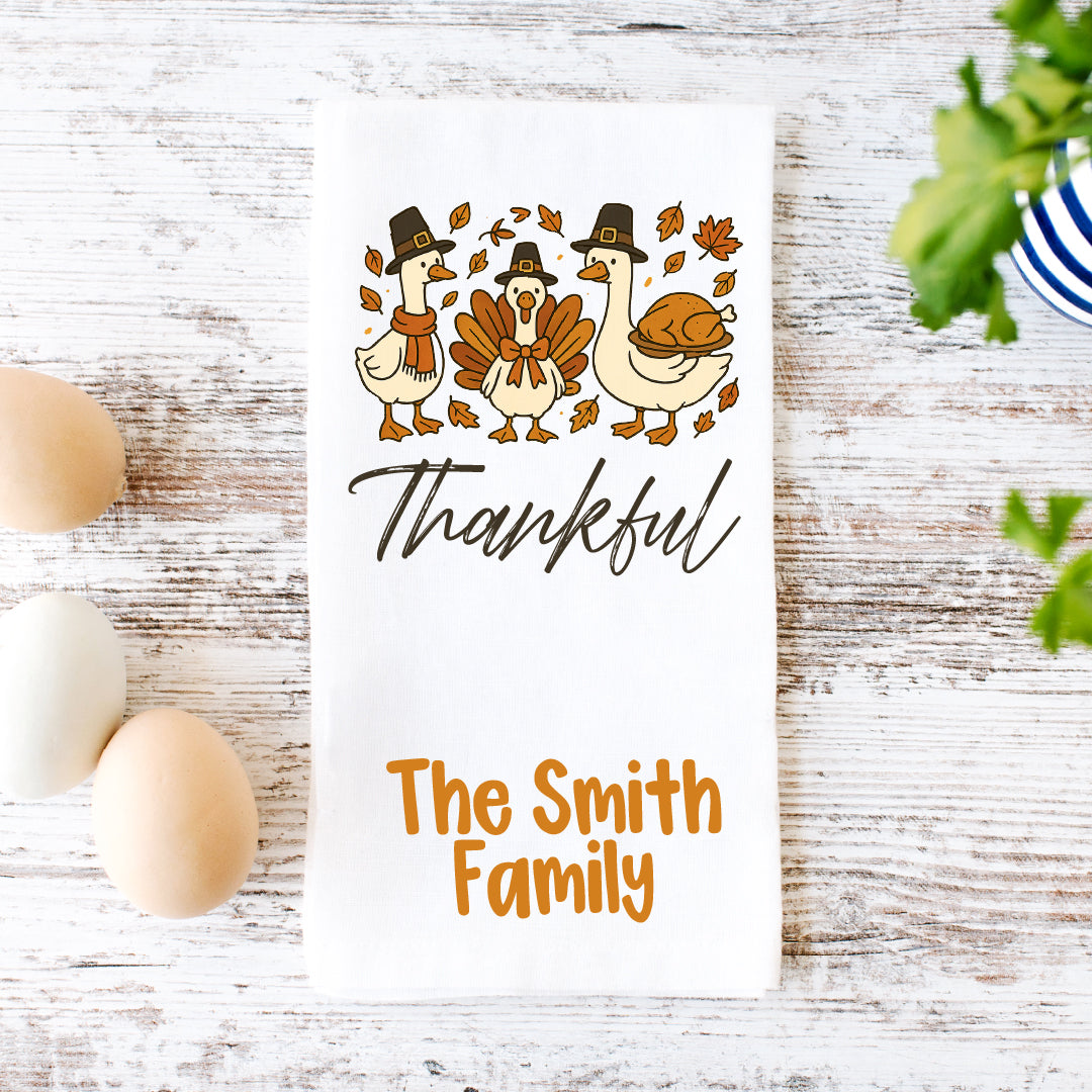 A white towel with a Thanksgiving-themed design, featuring three cartoon ducks and a turkey, along with the text "Thankful" and "The Smith Family".